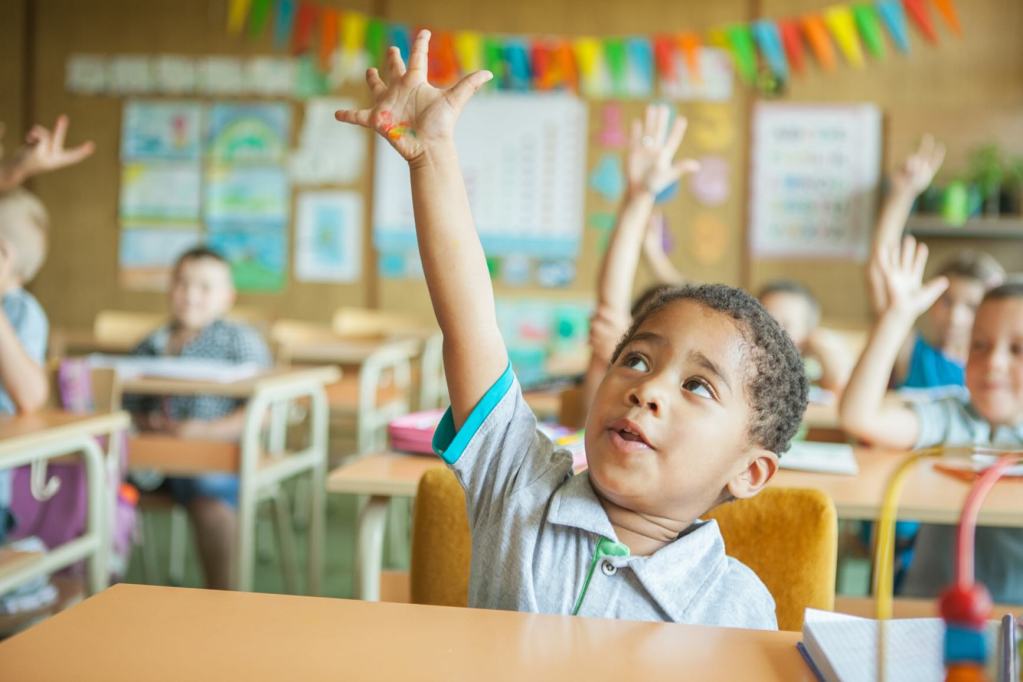 Primary school students raising hands to answer the teacher's question.